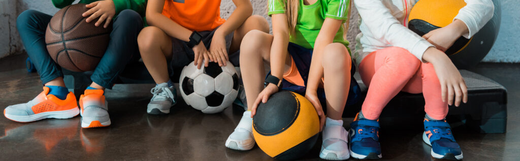 Cropped view of children sitting on step platforms with balls in gym, panoramic shot