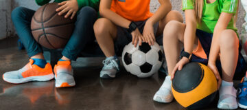Cropped view of children sitting on step platforms with balls in gym, panoramic shot
